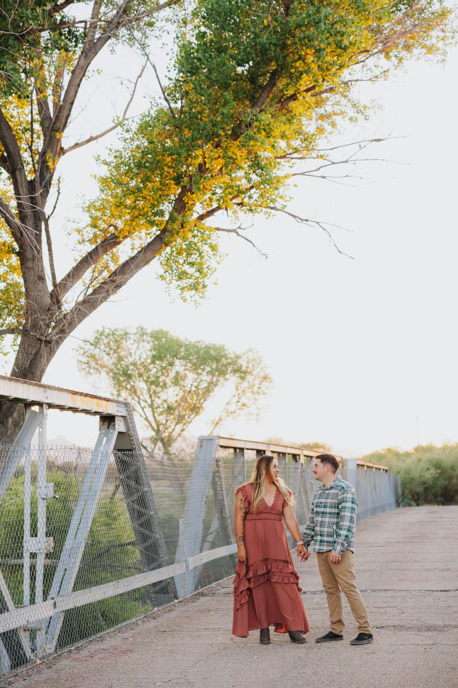 Couple walking on rustic bridge with autumn trees in background.