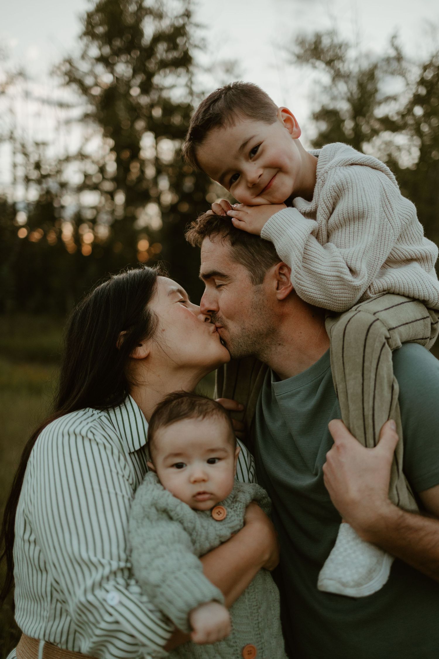 A family shares sweet moments together outdoors during golden hour in matching neutral tones.