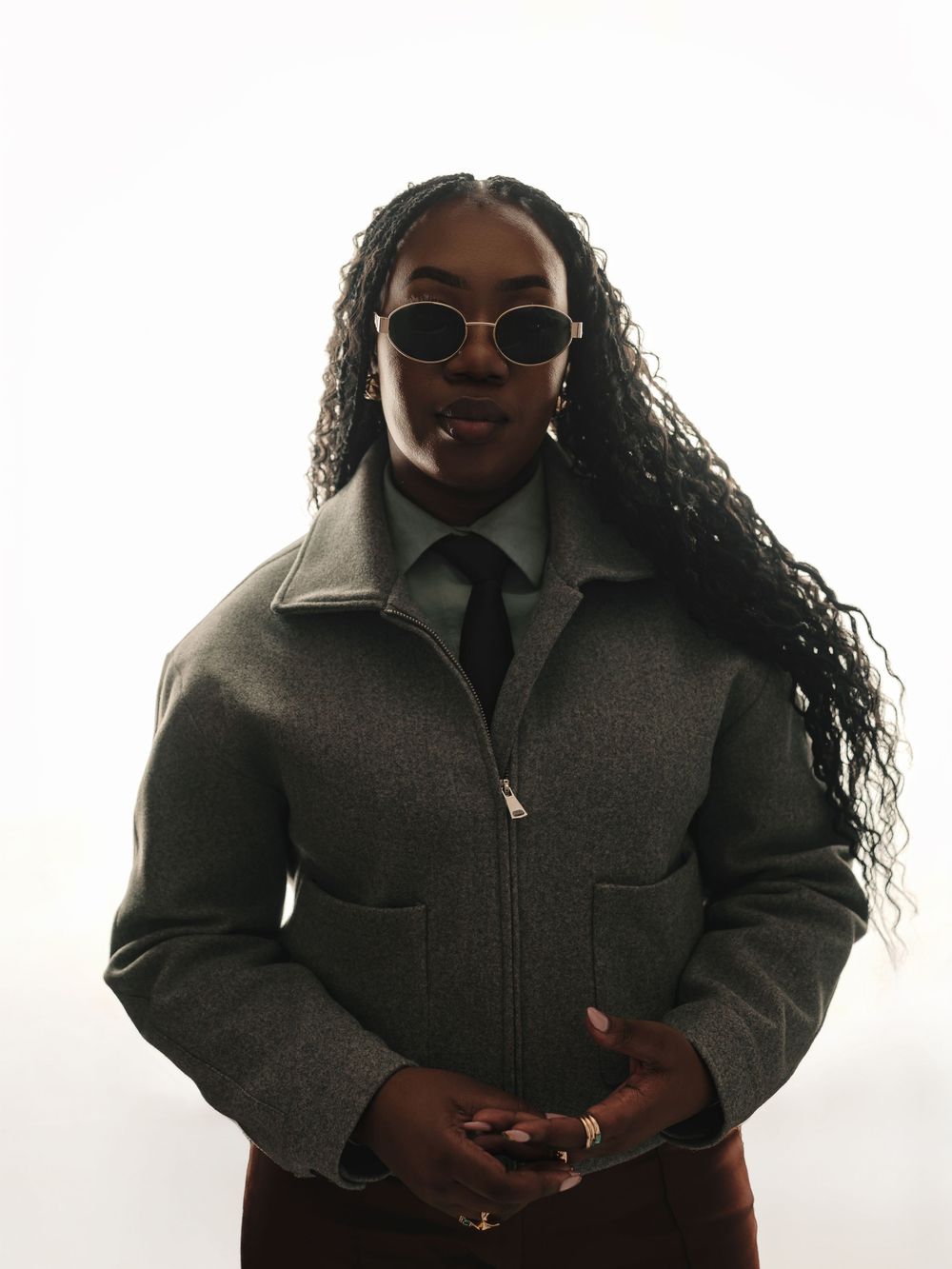 A person in a gray winter coat poses in front of a light background in a stylish portrait series.