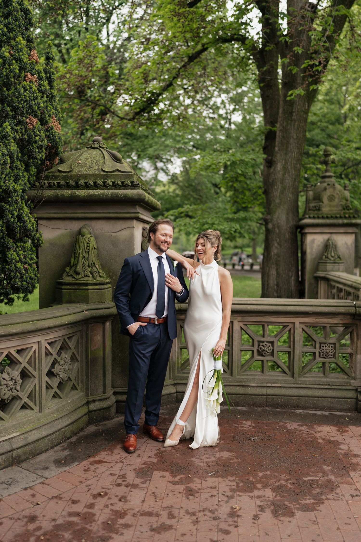 Elegant couple in formal wedding attire holding decorative fans against garden backdrop.