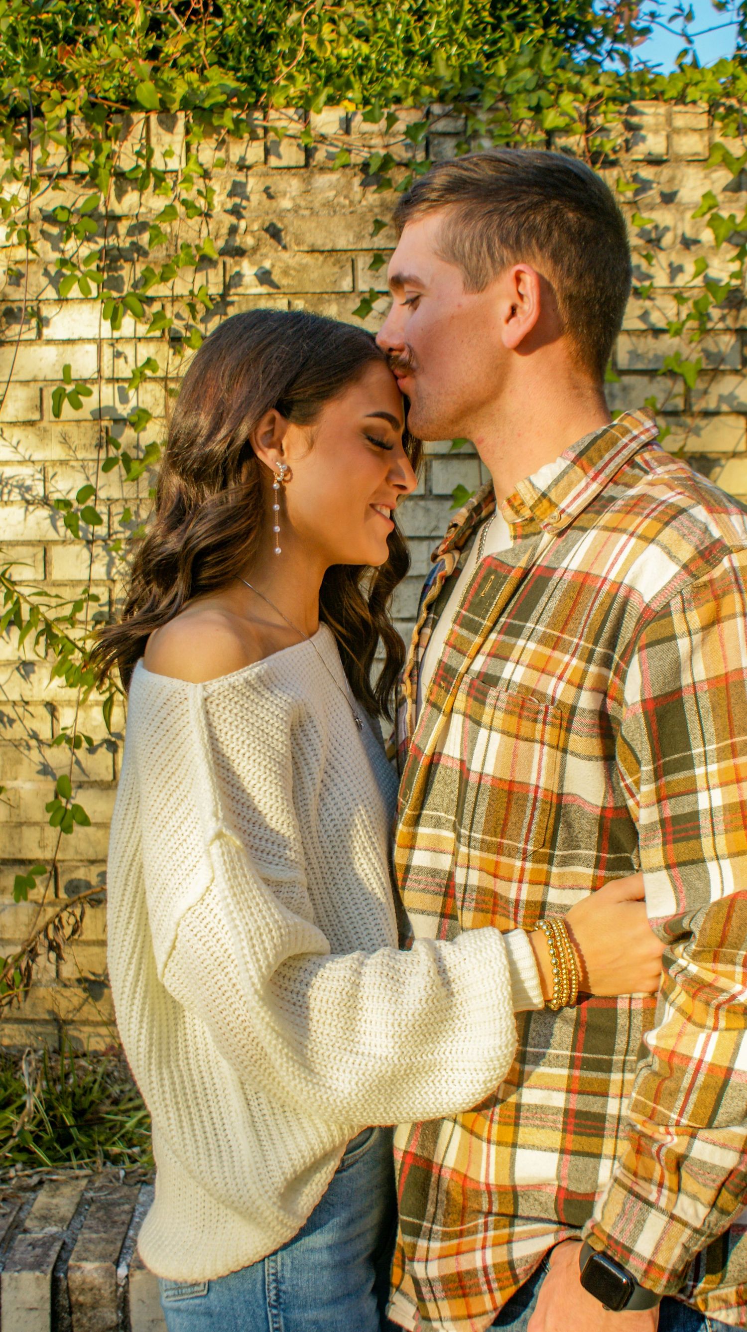 A tender moment between a couple against a brick wall with climbing vines in golden light.