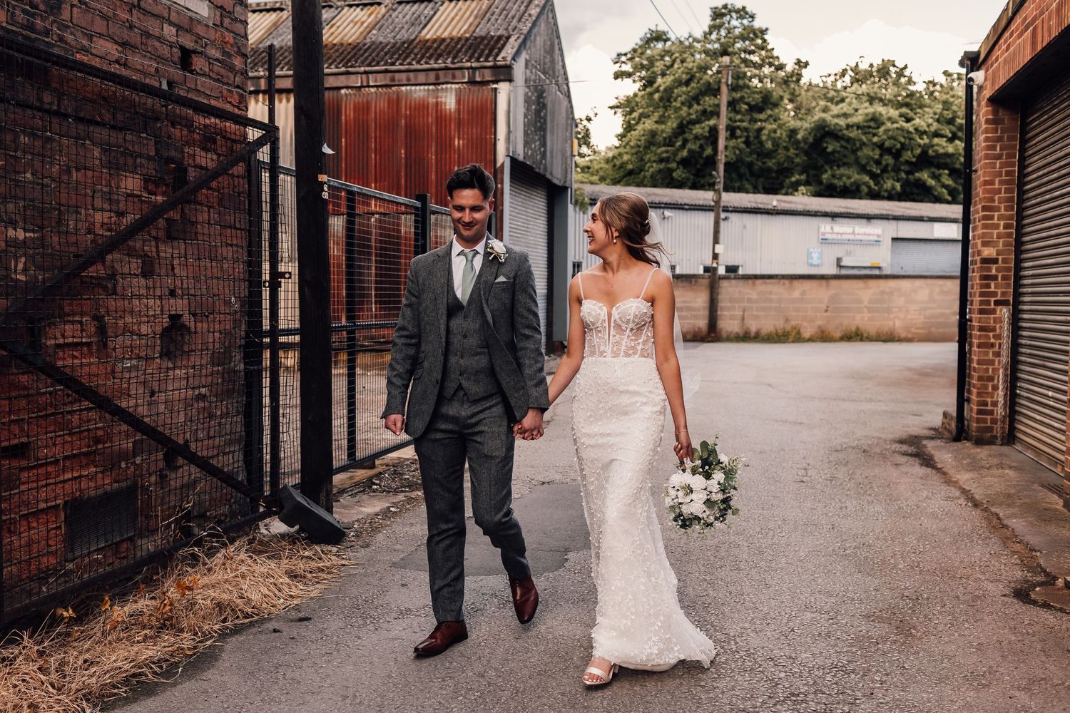 A couple walking along a brick pathway wearing elegant wedding attire.