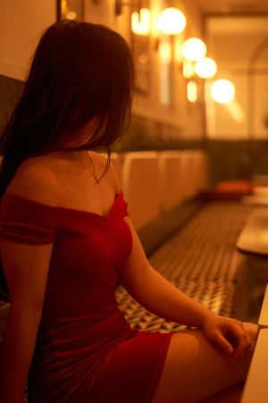 Person in red dress sits on a couch in moody lighting with glowing lanterns in background.
