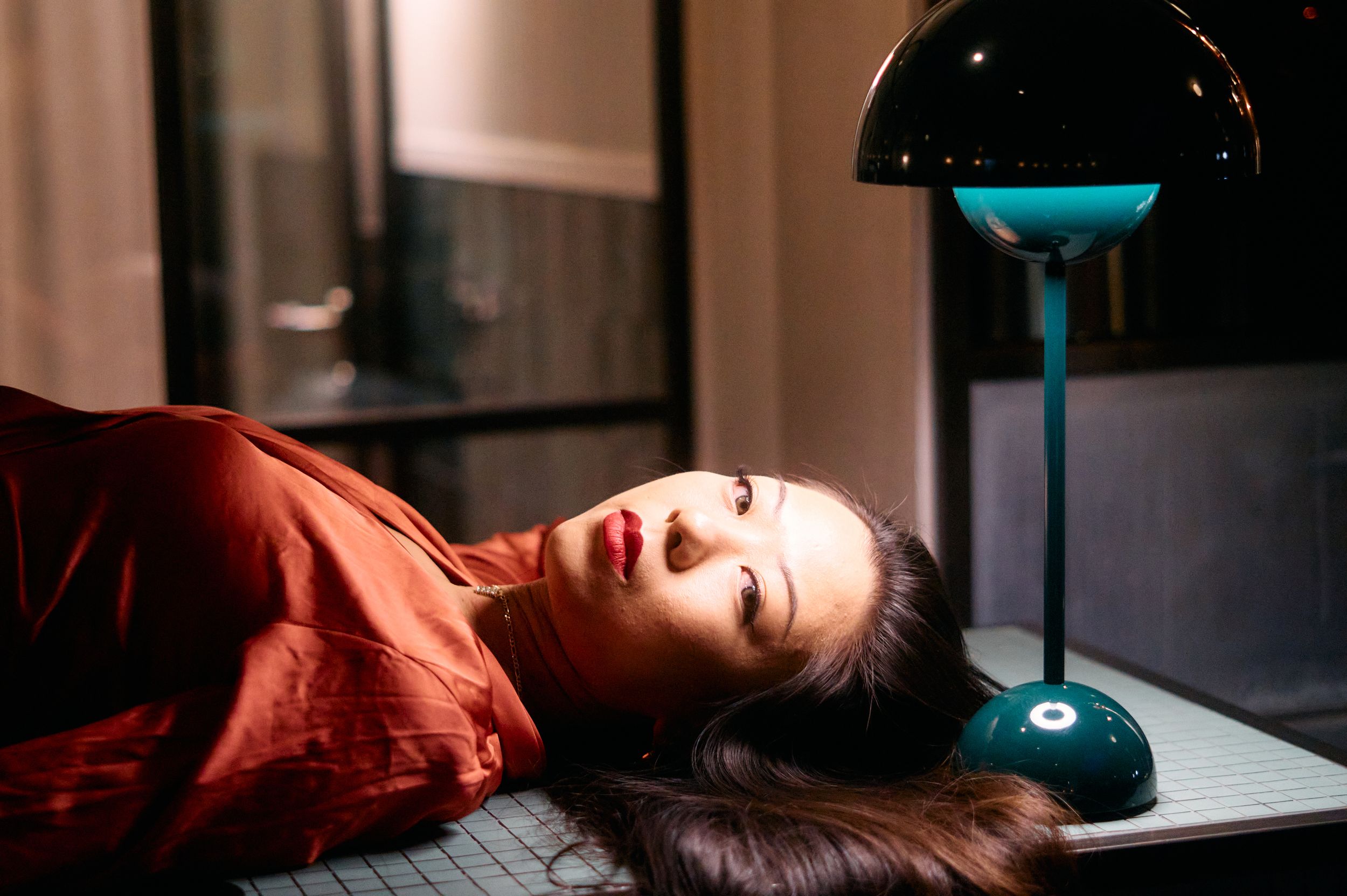 Person lying down with dark hair against black background under blue desk lamp.