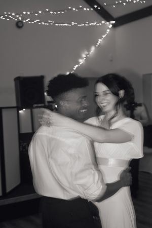 Black and white photo of a romantic first dance under string lights at a wedding reception.