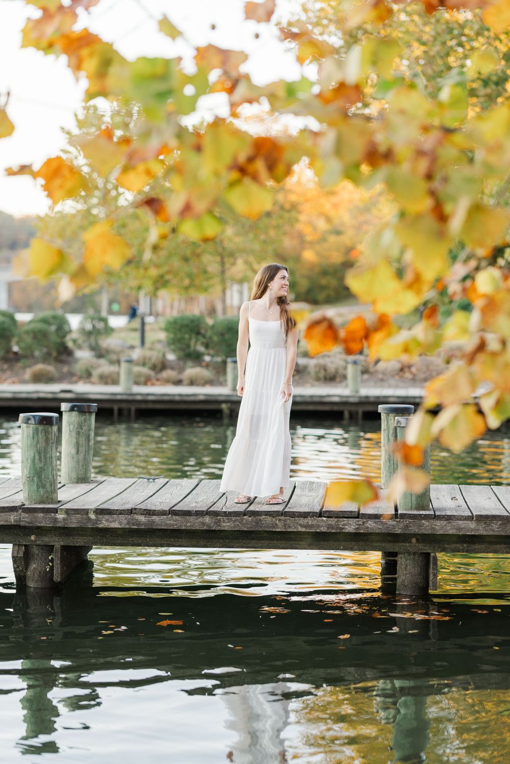 High School senior on the dock at Riverbend on the Occuquan River wearing a white dress in the fall with beautiful foliage.
