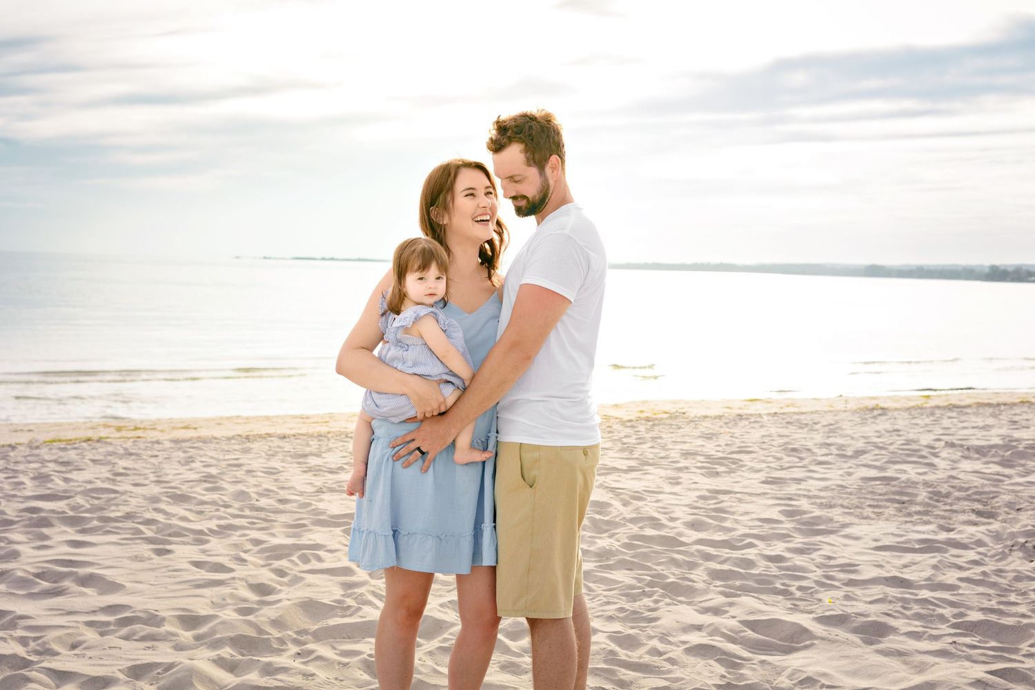 A family shares gentle moments together on a sandy beach during sunset, walking and embracing by the lake.
