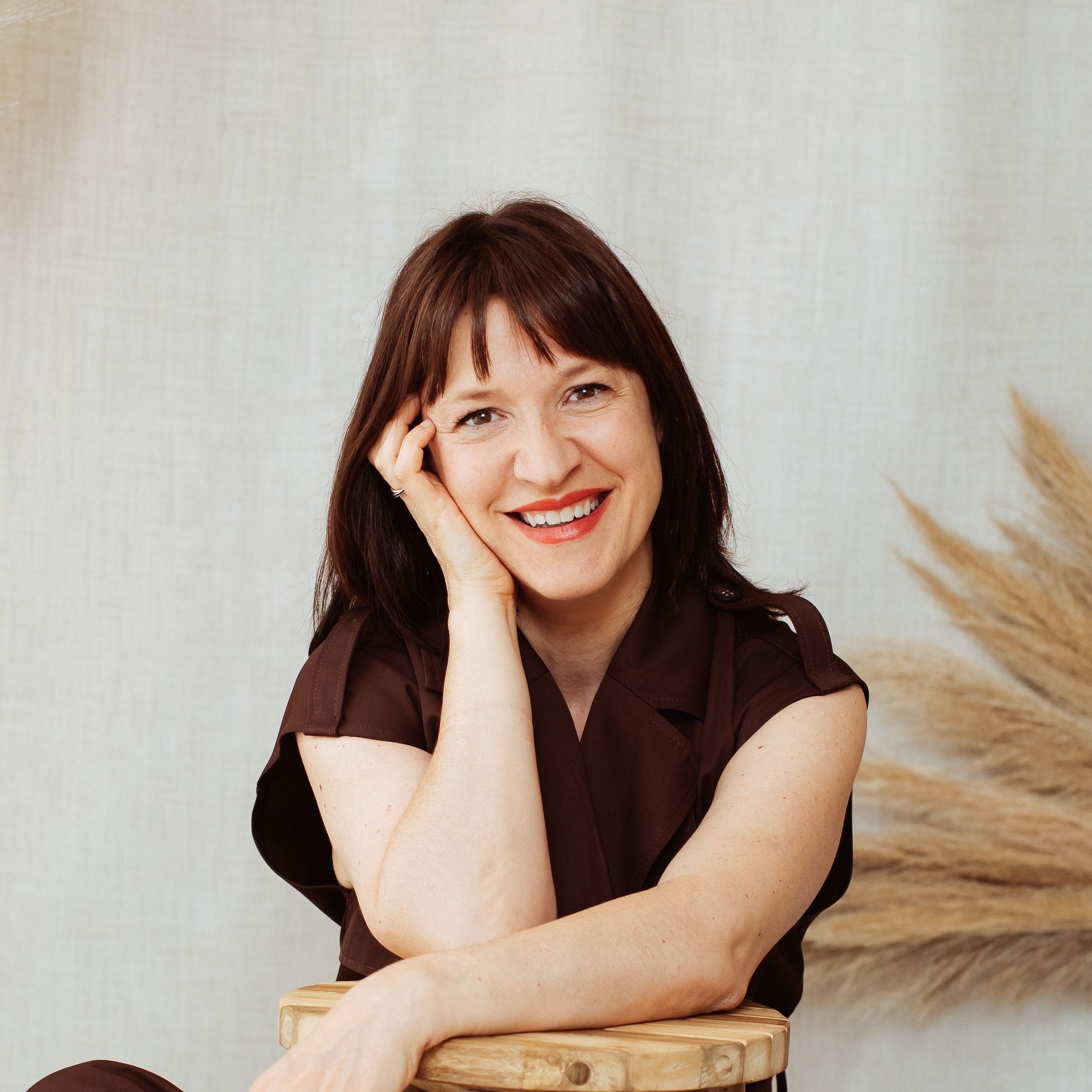 Portrait session with dried pampas grass and wooden stool against white backdrop.