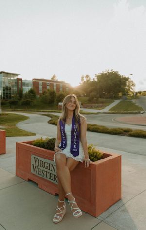 Graduate in white dress and graduation sash sits at a Virginia Wester planter during golden hour.