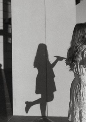 Artistic black and white silhouette of a person in a dress casting a playful shadow on a wall.