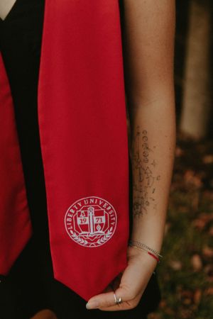 Close-up of a red graduation tie with university seal and a tattooed arm.