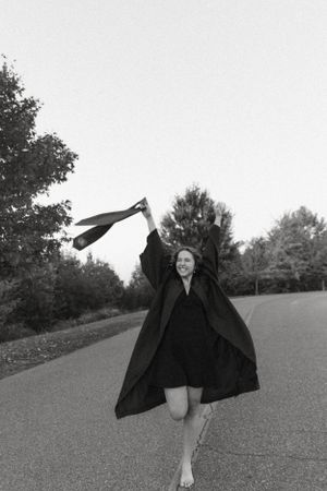 Black and white photo of a graduate celebrating by tossing their tie in the air outdoors.