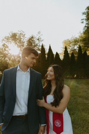 A couple shares a joyful moment in a garden with evergreen trees during golden hour sunset.
