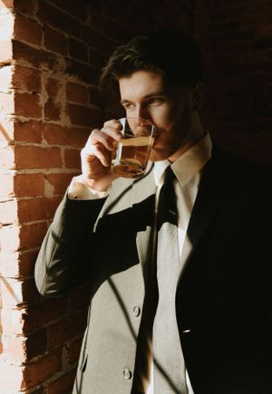 Moody portrait of a person sipping a drink against exposed brick wall with dramatic lighting.