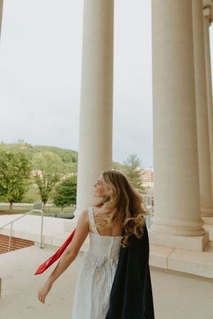 White dress and graduation stole movement captured between classic architectural columns.