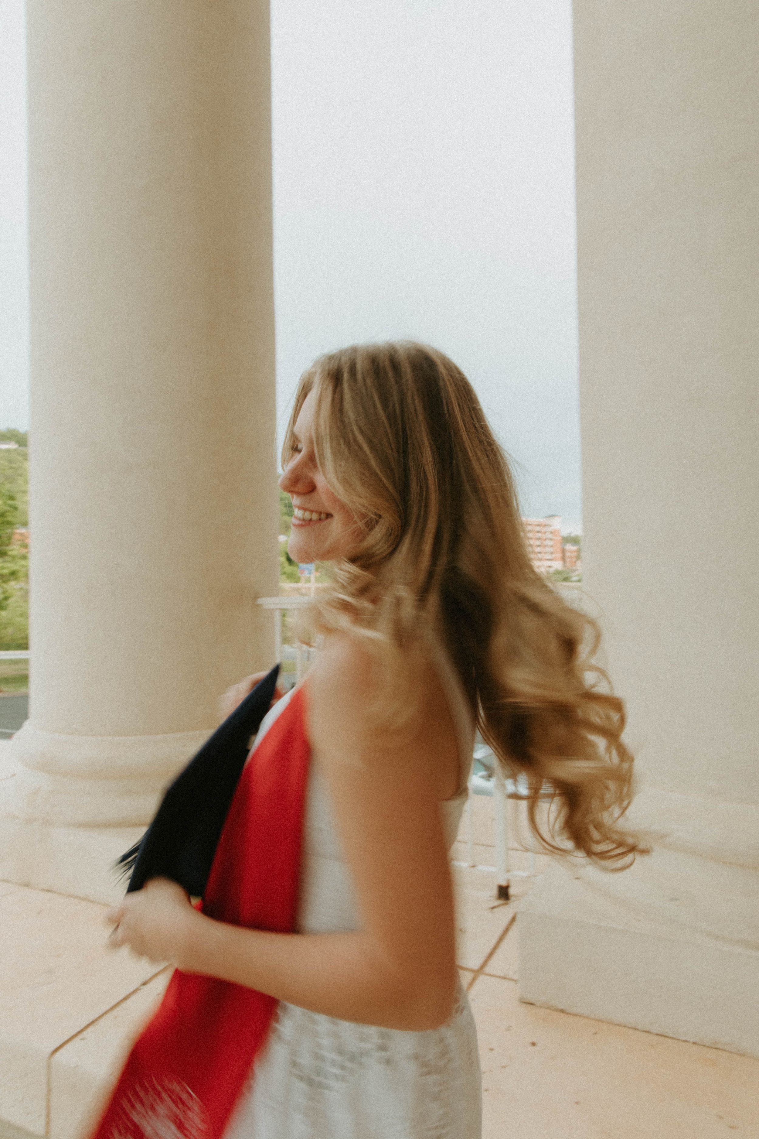 A joyful portrait between classic white columns with red and black graduation attire.
