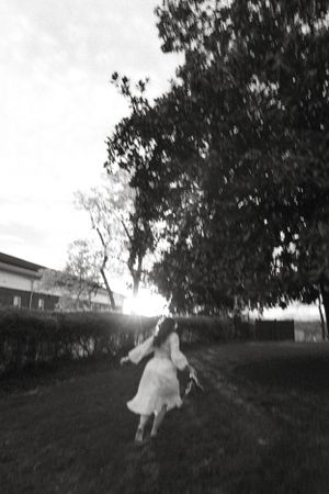 Black and white photo of a person spinning in a flowing dress against a sunlit outdoor backdrop.