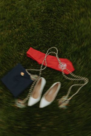 A blurred photo of a red graduation stole, navy purse, and white heels arranged on grass.