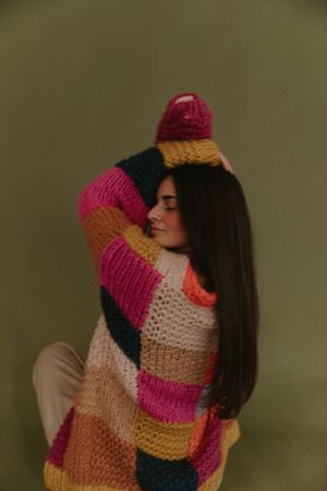Artistic portrait featuring a colorful striped knit sweater against a dark background.