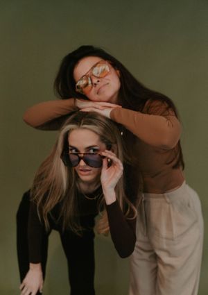 Playful studio portrait with two friends wearing sunglasses in brown tones.