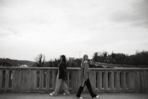 Black and white photo of two people walking along a stone balustrade.