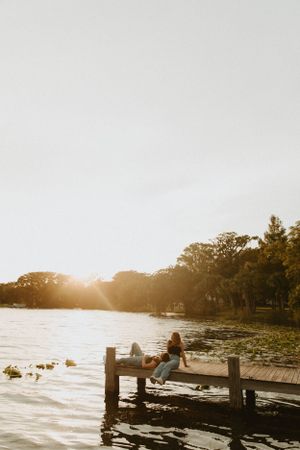 Silhouette of person sitting on wooden dock at sunset overlooking peaceful lake.