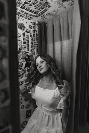 Black and white portrait in white dress against wall covered in photographs.