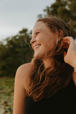 Golden sunlit portrait of a young woman smiling and touching her hair outdoors.