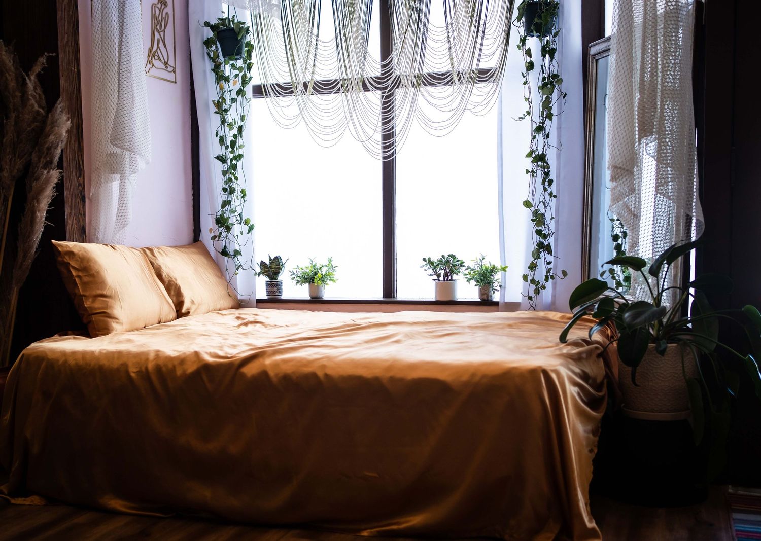bed by a window with plants and champaign color satin sheets