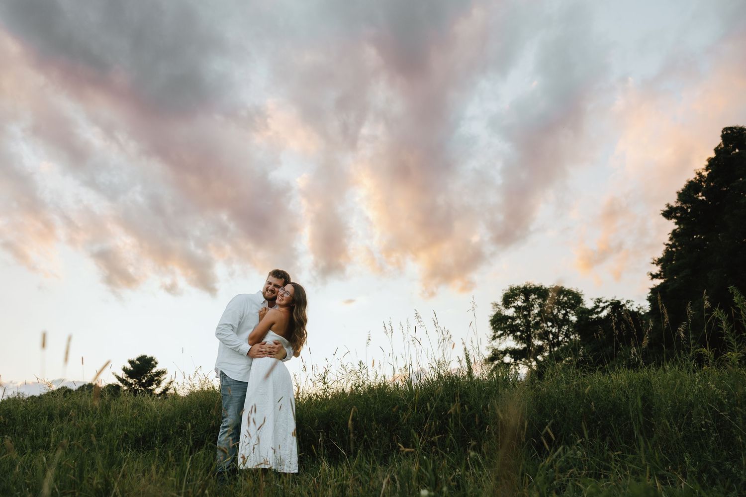 Couple in coordinated neutral outfits share tender moment in field during golden hour.