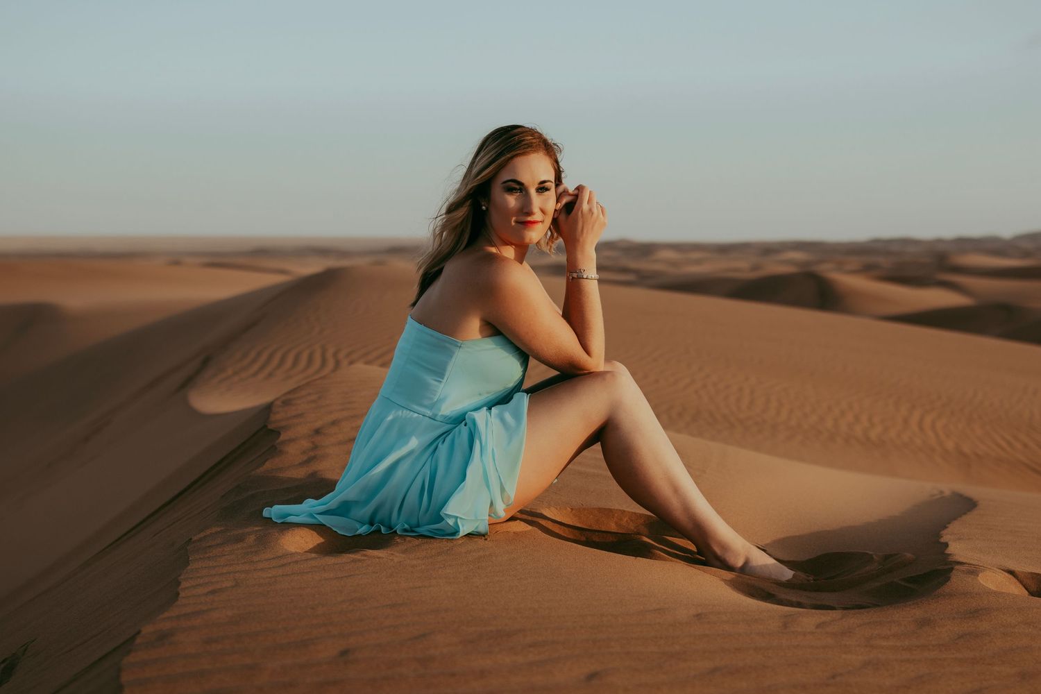 A beautiful girl in a little blue dress sitting gracefully in the Namib Desert dunes near Swakopmund, with golden sand stretching behind he