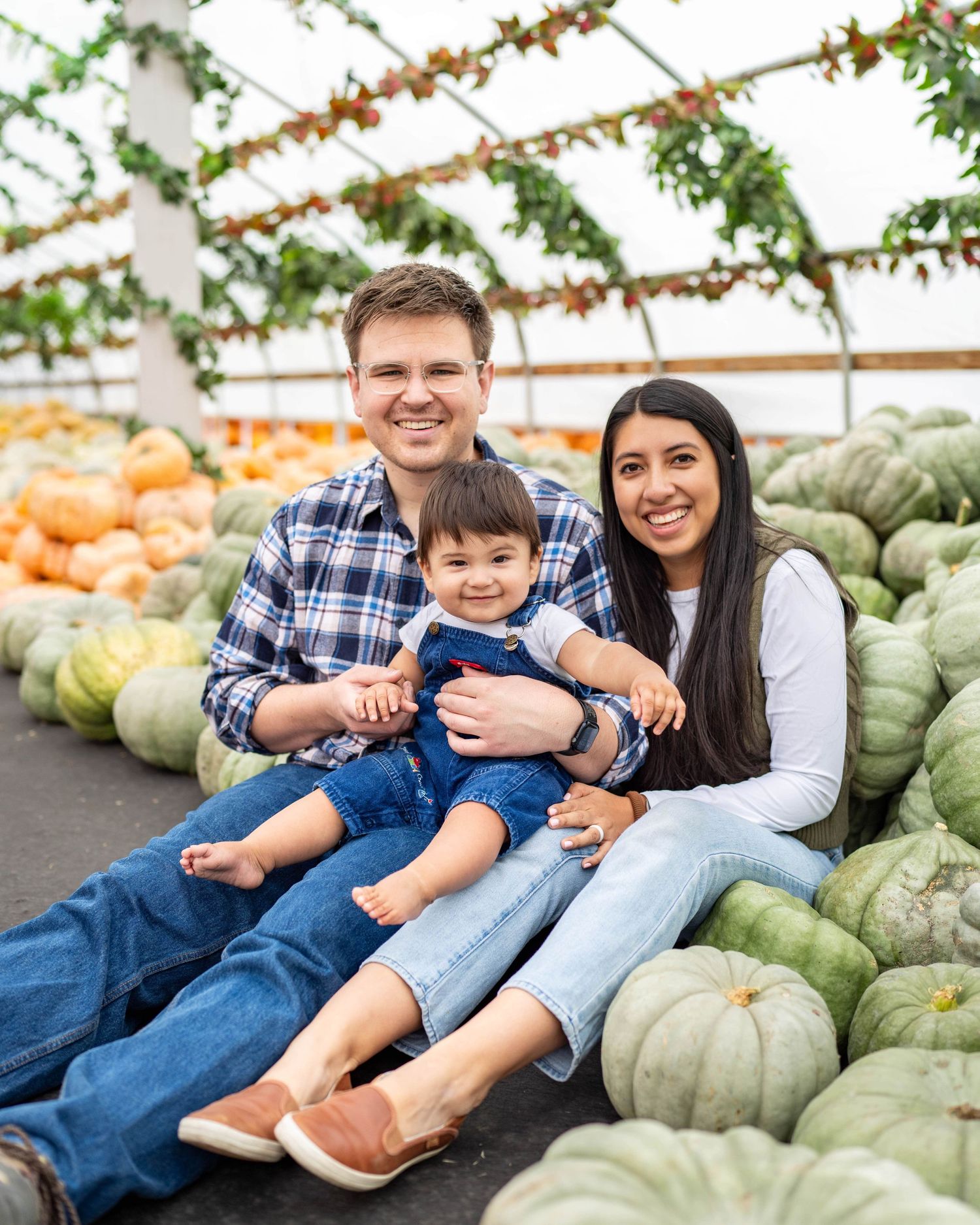 Family sitting together among green and orange pumpkins at autumn harvest market at Kuwahara's in Draper.