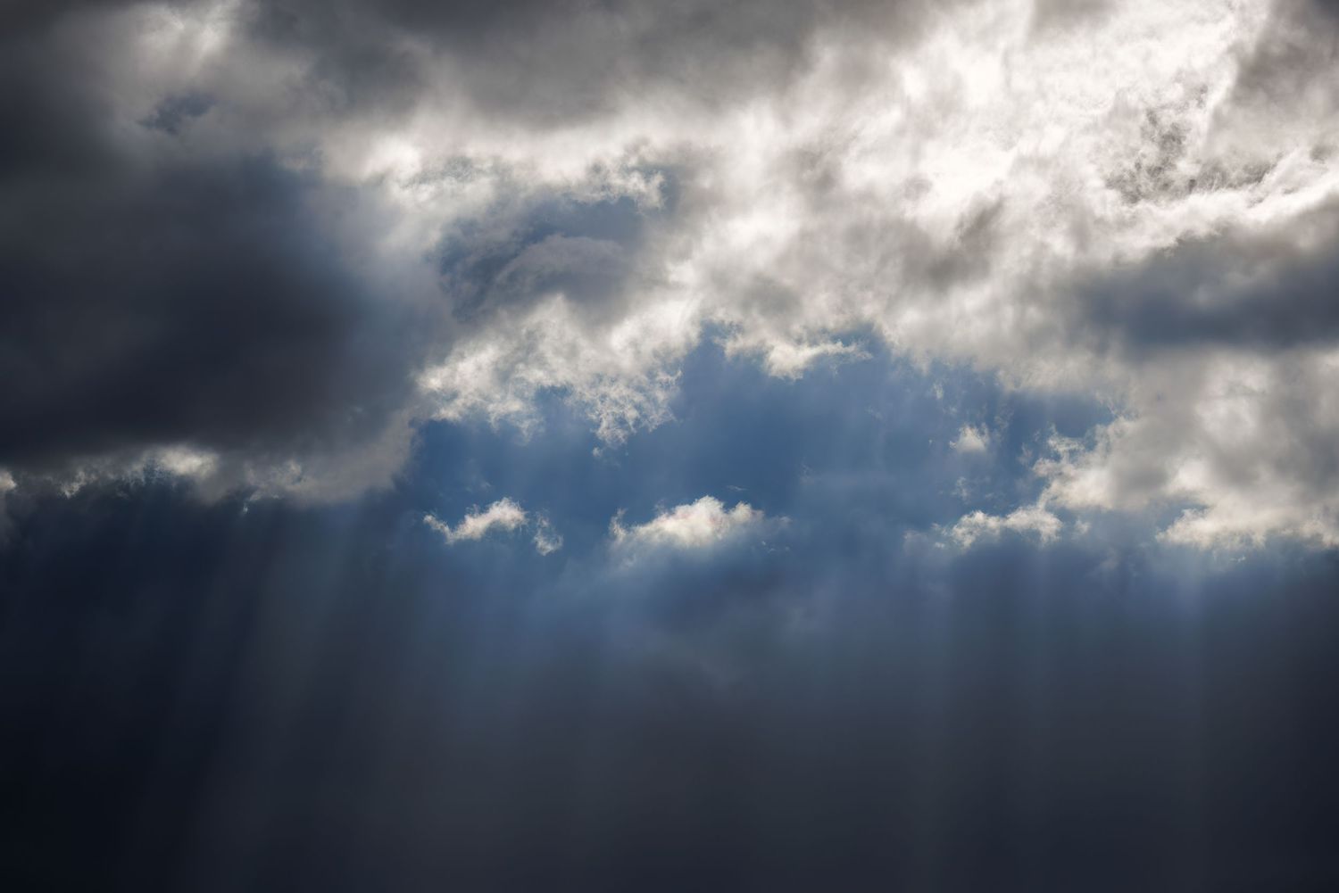 Dramatic storm clouds with sunbeams breaking through gray sky.
