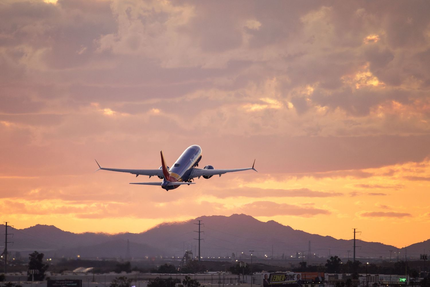 Airplane taking off at sunset with dramatic pink and purple sky over mountain silhouettes.