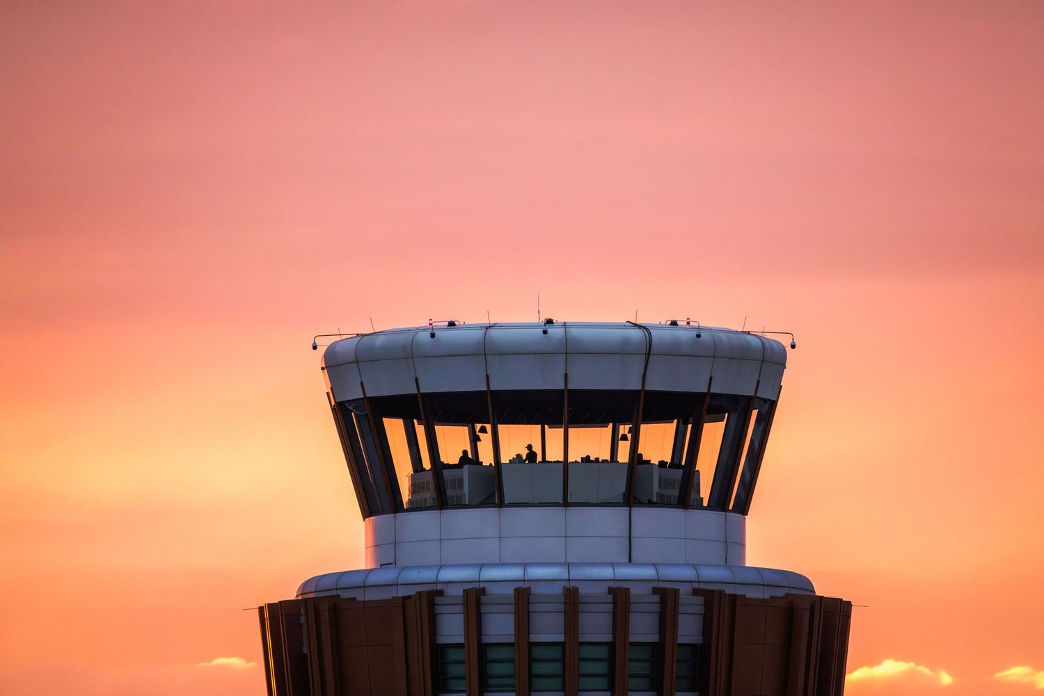Air traffic control tower silhouetted against a vibrant orange and pink sunset sky at an airport.