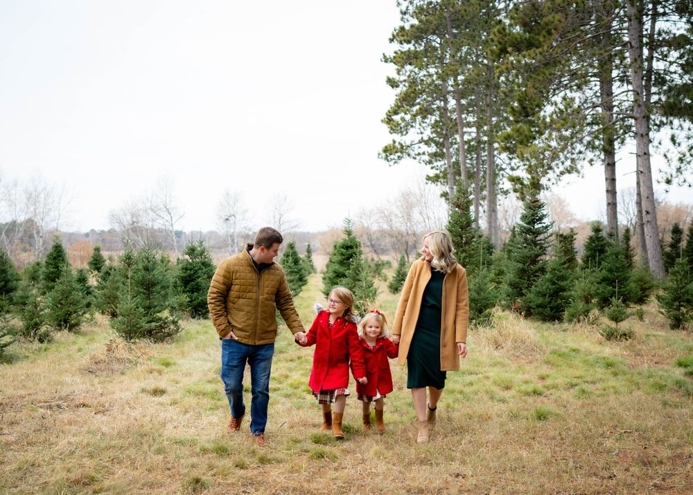 Family walking through Christmas tree farm holding hands.