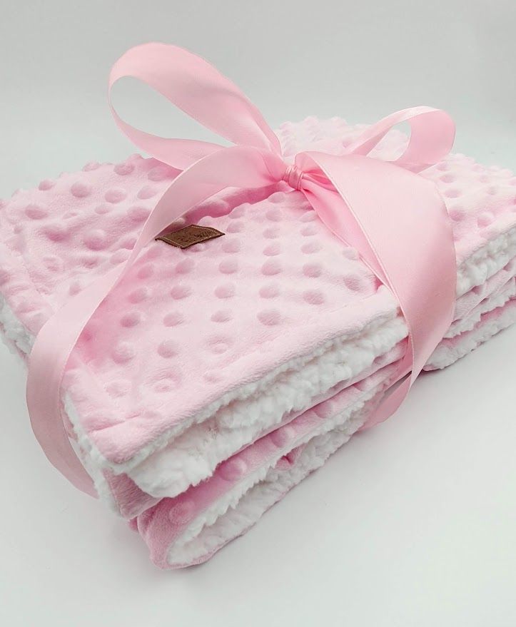 Soft pink minky dot baby blanket with white backing tied with a delicate pink satin ribbon.