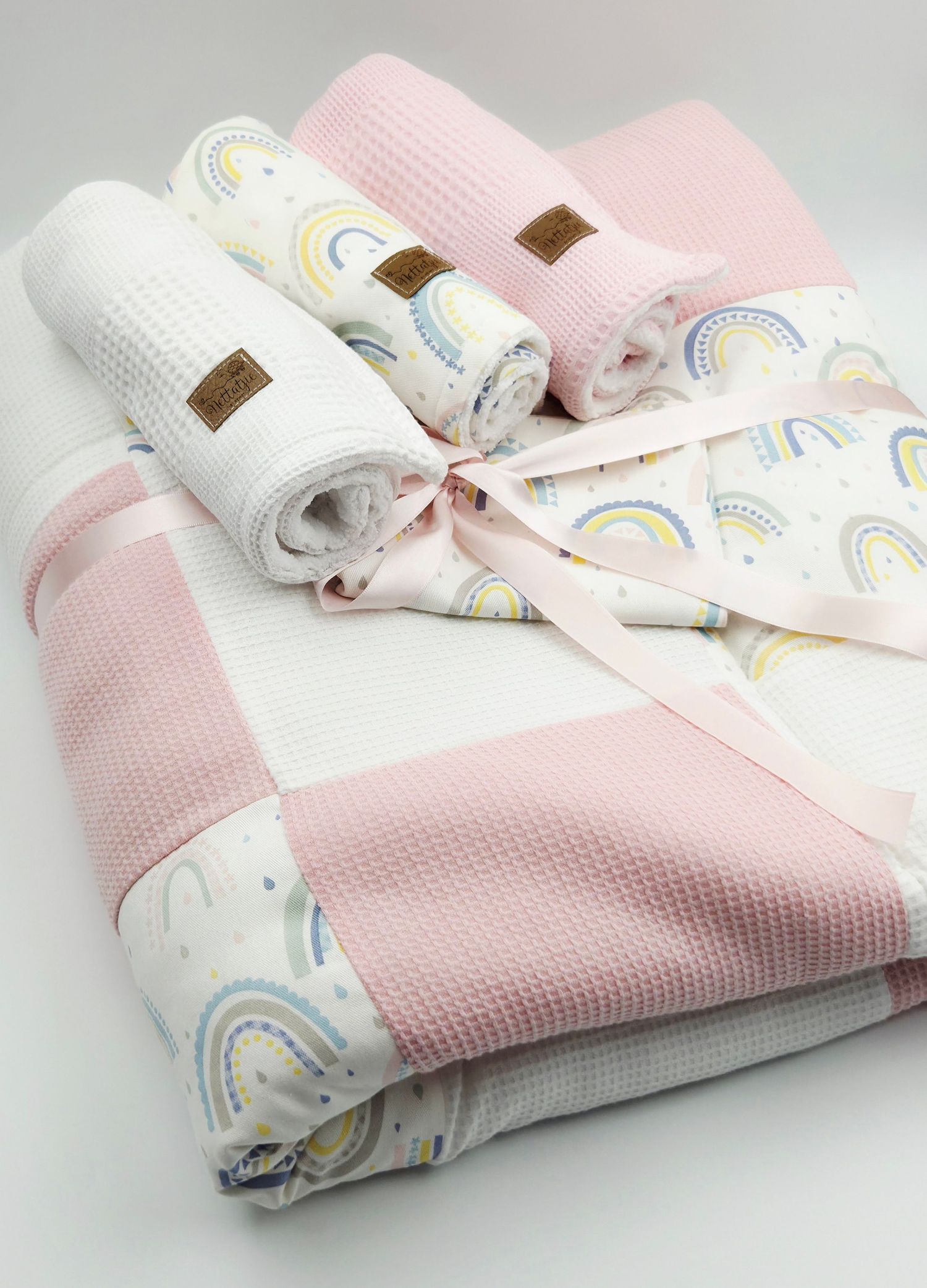 Rolled baby blankets in pink and white with delicate rainbow patterns and ribbon tie.
