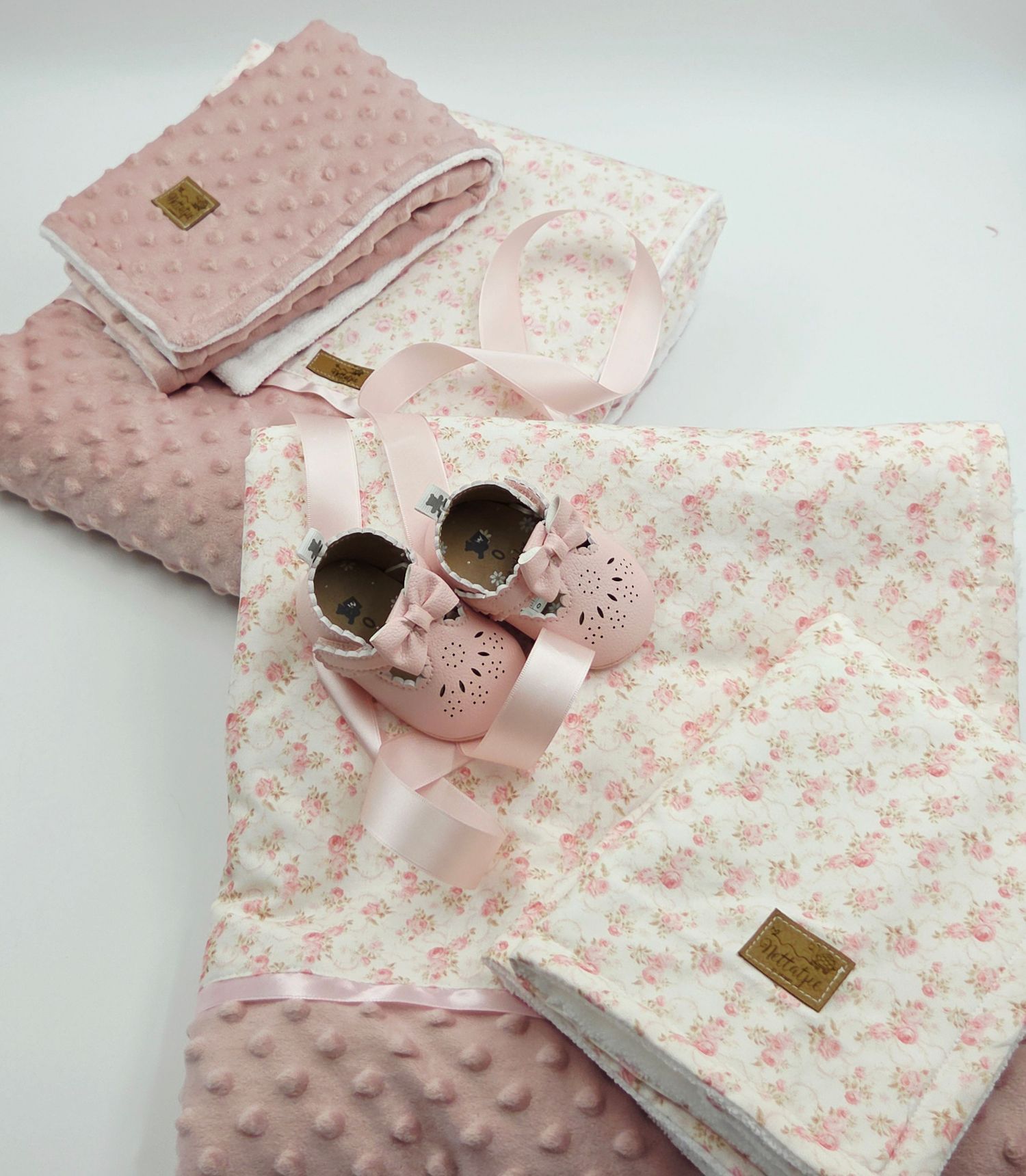 Pink baby blanket set with floral pattern and matching shoes displayed on white surface.