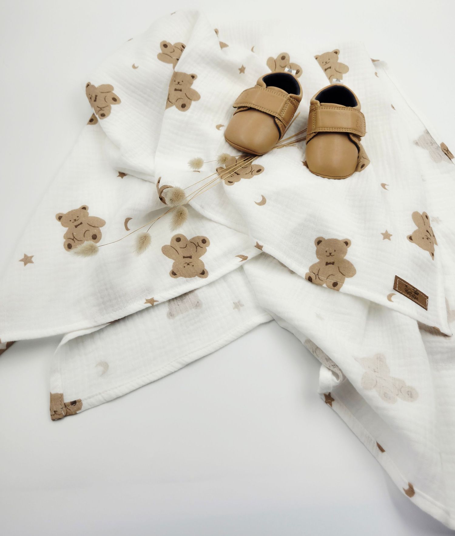 White fabric with teddy bear print pattern and tan baby shoes.