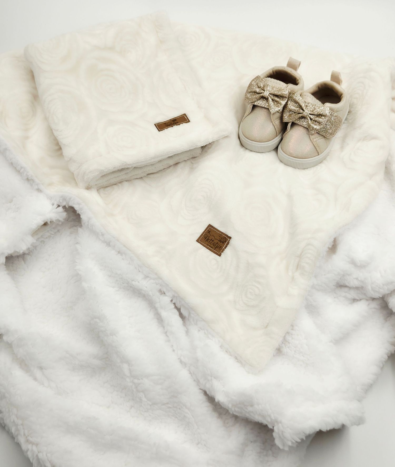 Soft white plush baby blanket with cream colored shoes and bow detail.