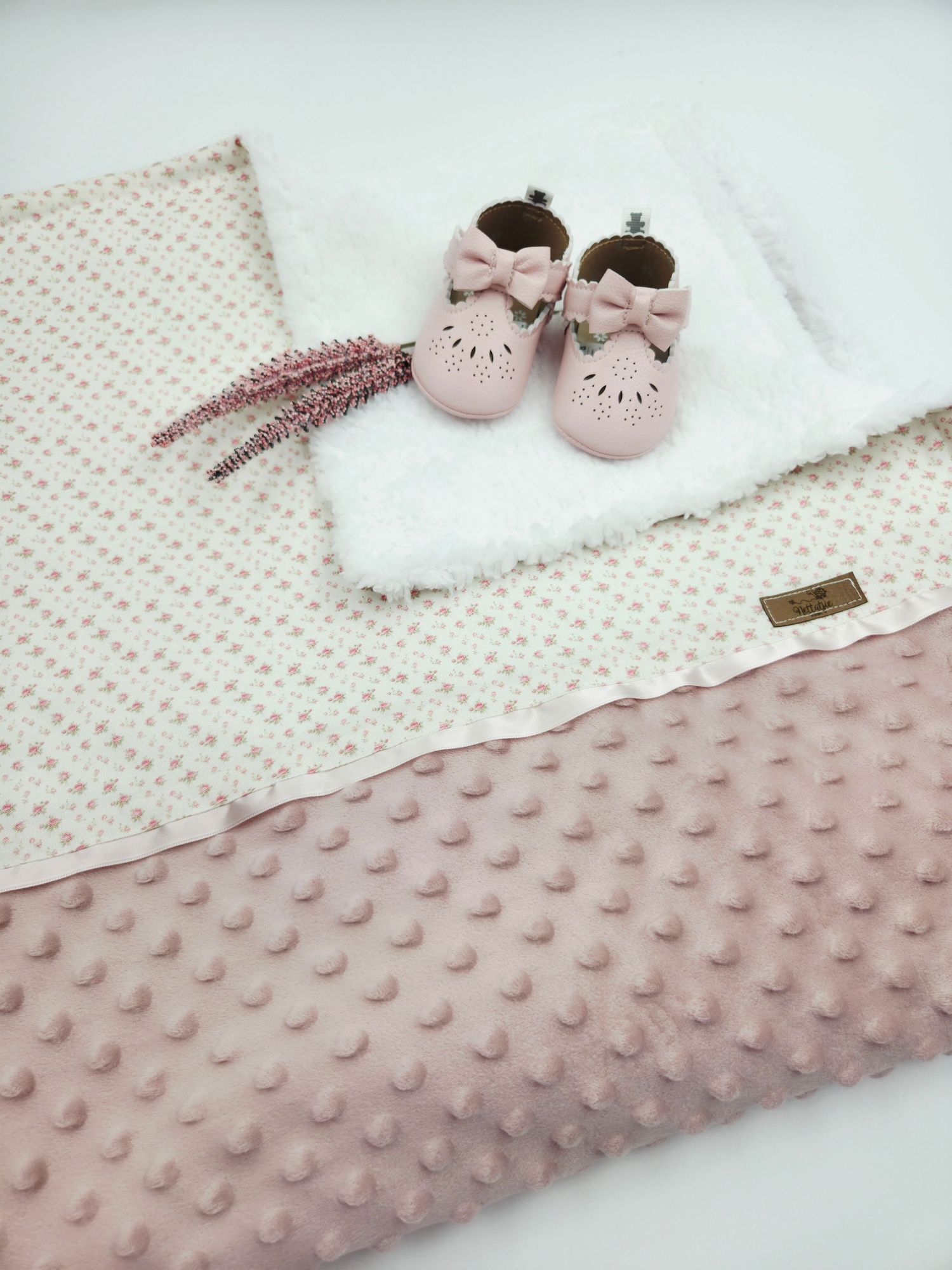 Pink textured blanket with floral pattern and tiny pink shoes.