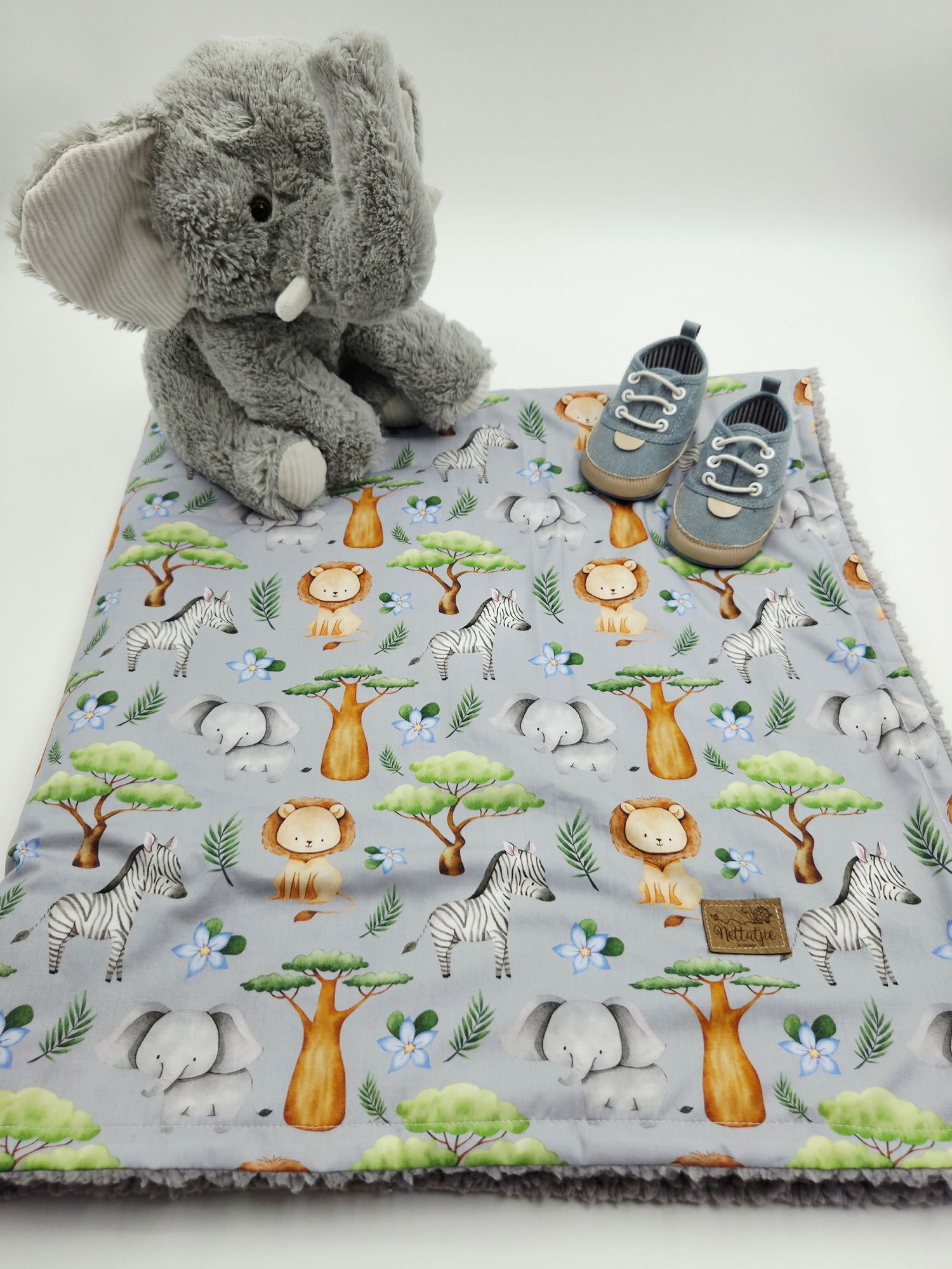 Safari animal print baby blanket with gray plush elephant toy and shoes on white surface.