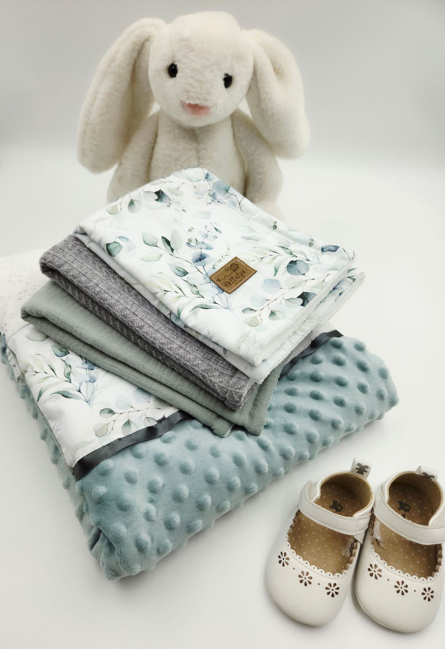 Soft mint green baby blanket set with plush bunny toy and white leather shoes.
