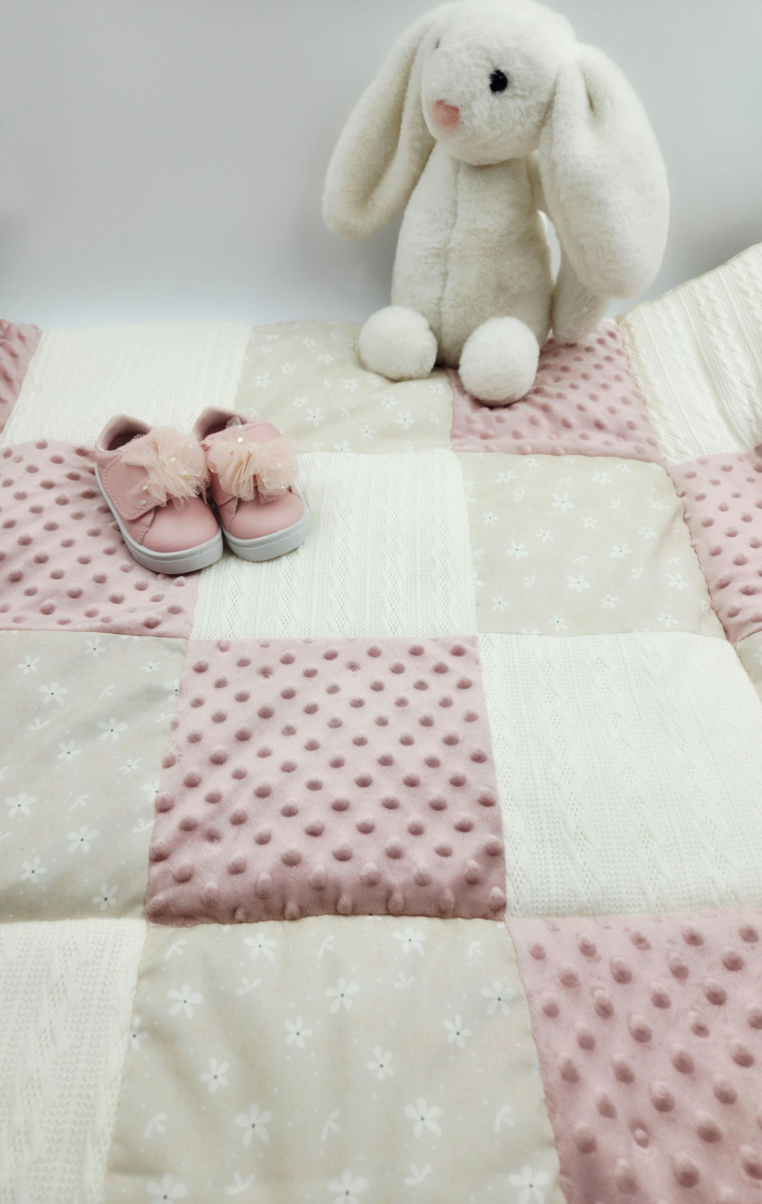Pink and white patchwork baby blanket with plush bunny and matching shoes.