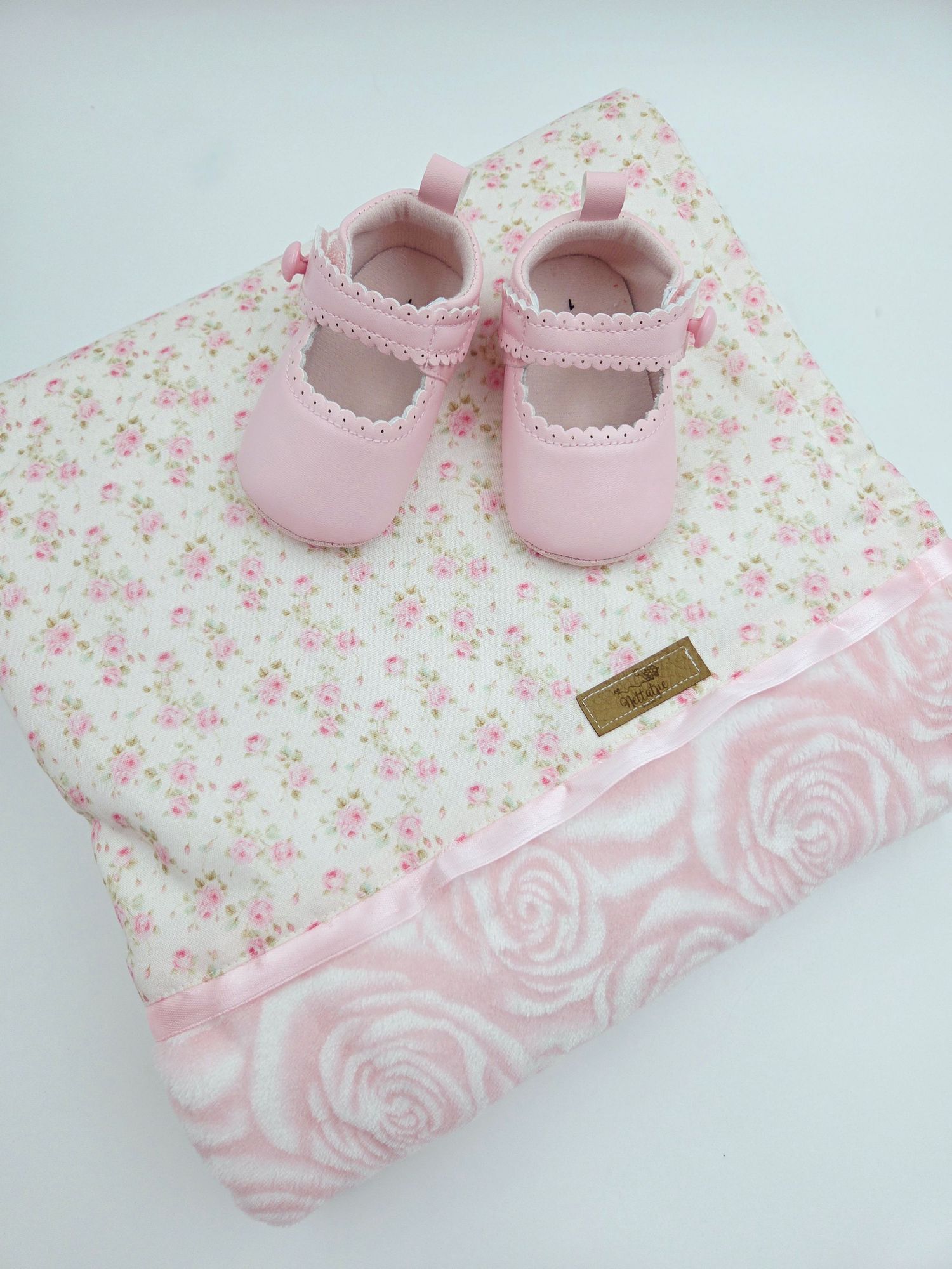 Delicate pink floral blanket with rose pattern and matching baby shoes.