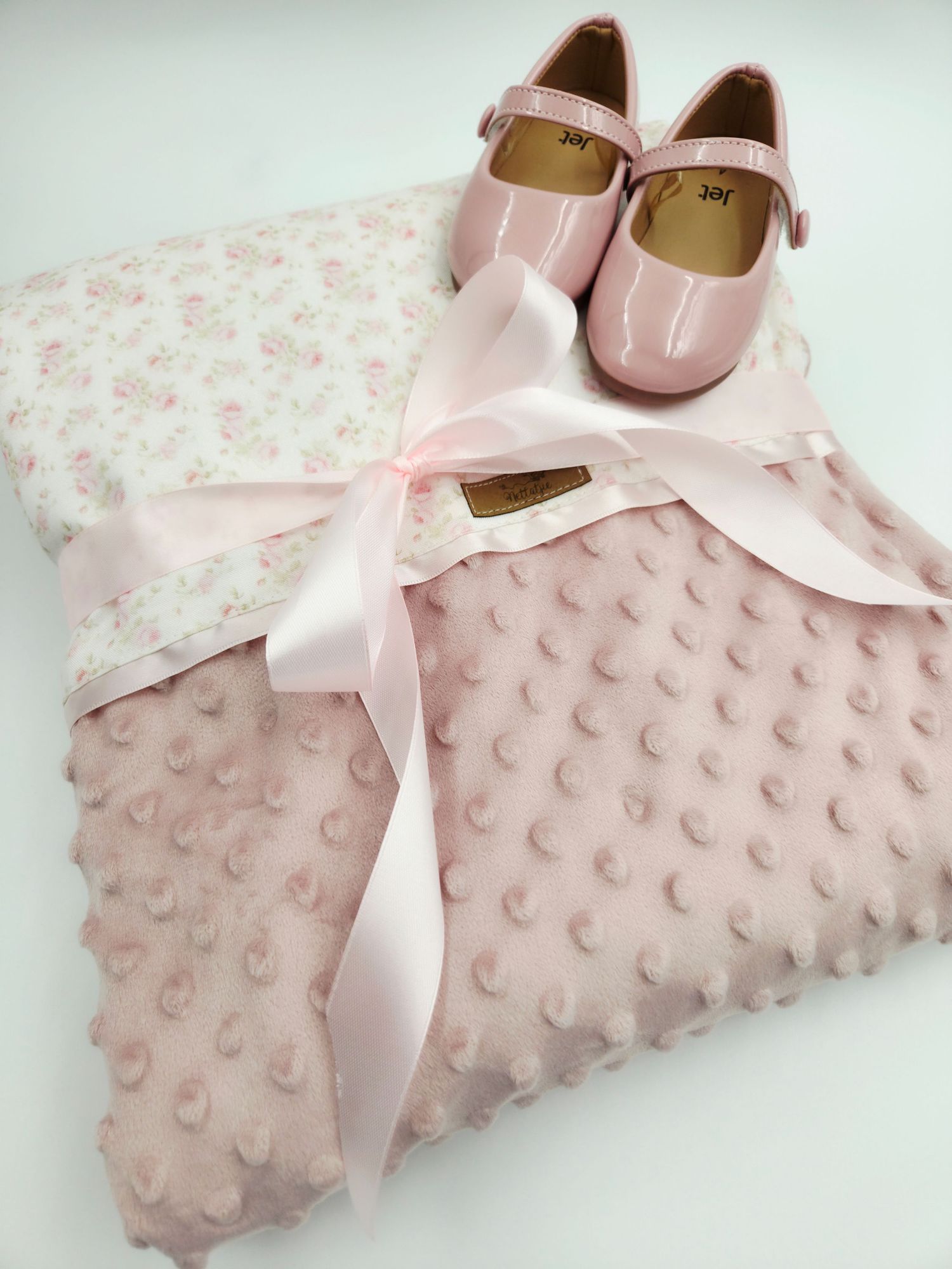 Pink minky dot blanket with satin bow and baby shoes arranged elegantly.
