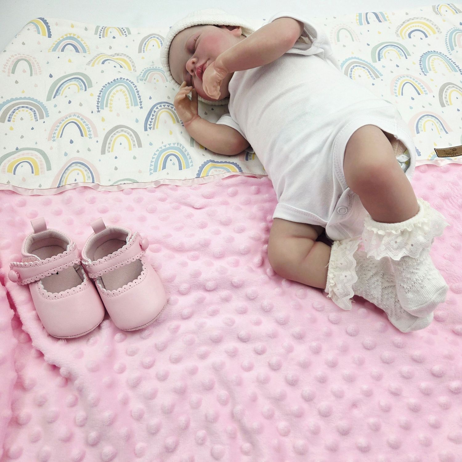 Pink minky dot blanket with small pink shoes and rainbow pattern background.