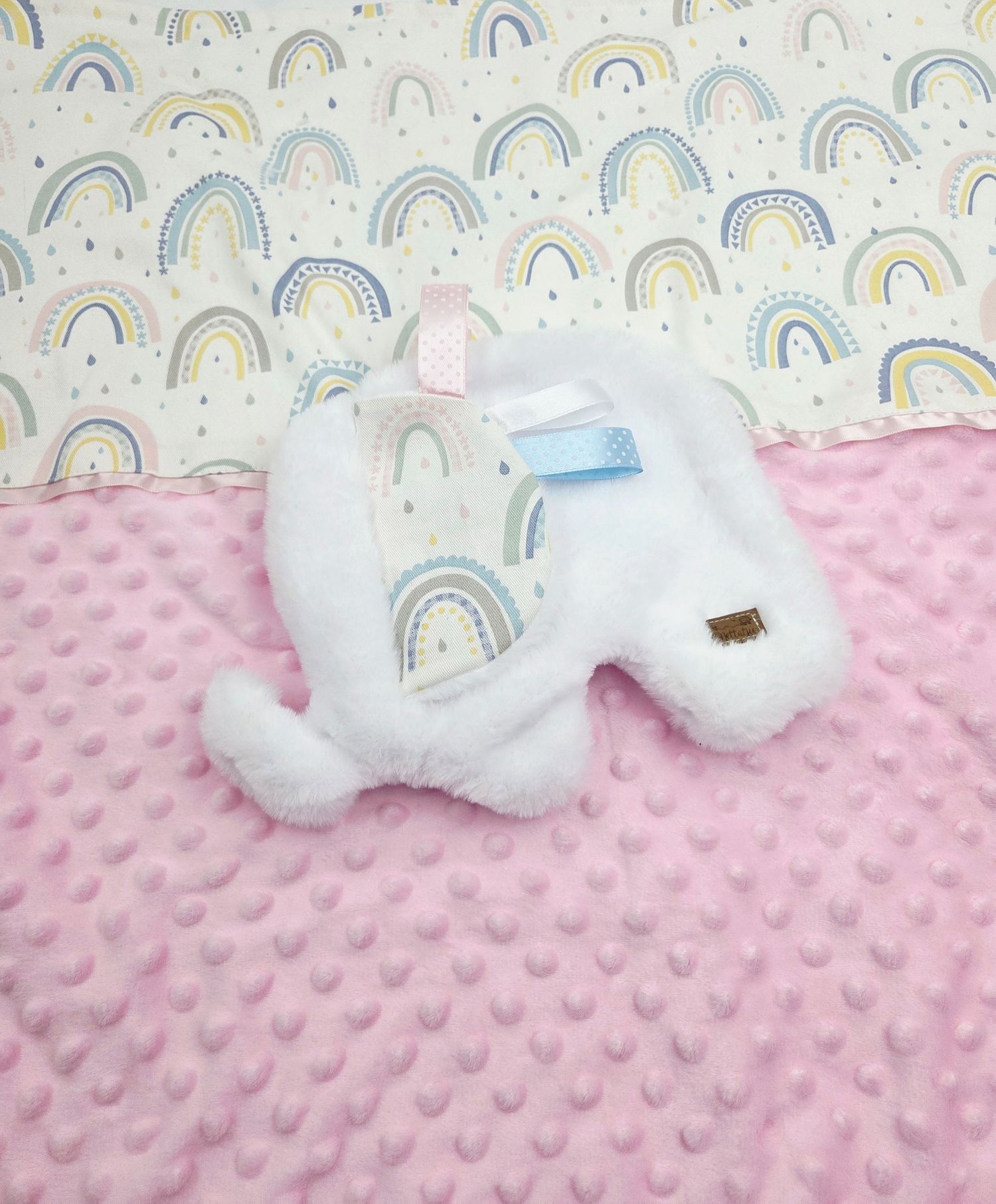 White plush toy on pink minky dot blanket with pastel rainbow pattern background.