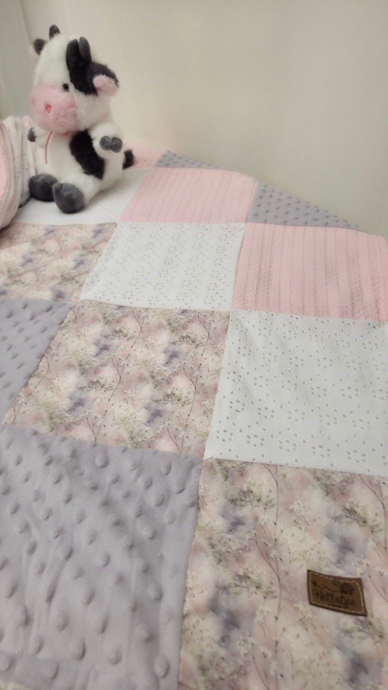 Pink and gray patchwork baby quilt with floral and minky dot fabric squares, displayed with a black and white cow stuffed animal.